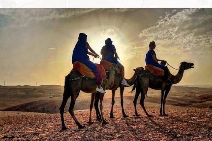 Three people riding camels in a desert landscape with a sunset in the background. 5