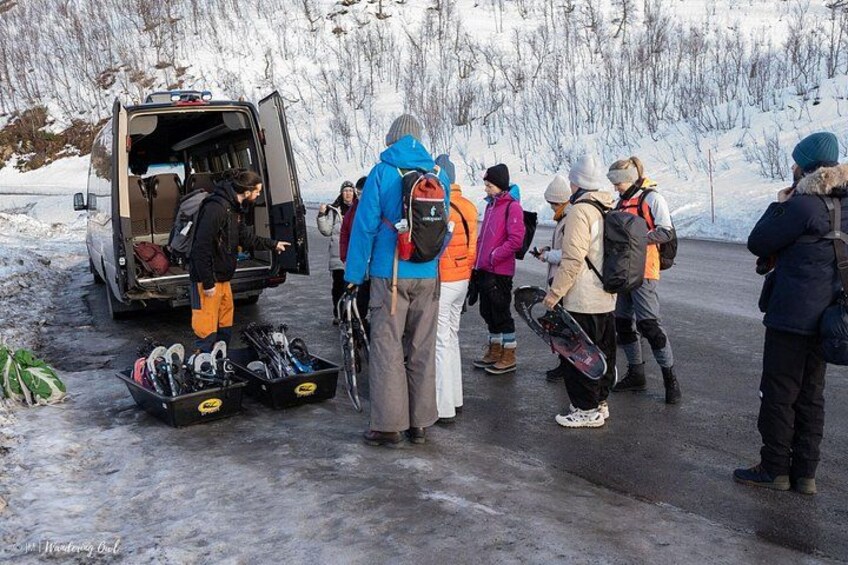 A group of people with backpacks and skis gathered around a van on a snowy road. 3