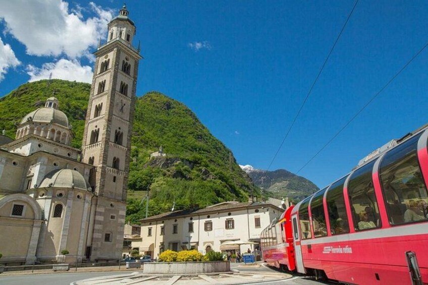 A red train, a church with a bell tower, and a mountainous landscape. 5