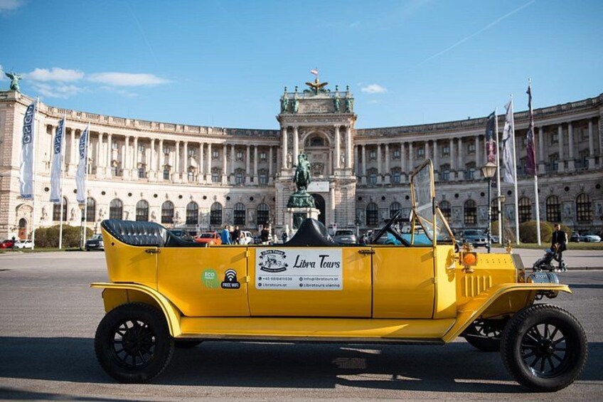 Un coche amarillo antiguo estacionado frente a un edificio histórico grande con columnas y una estatua. 1