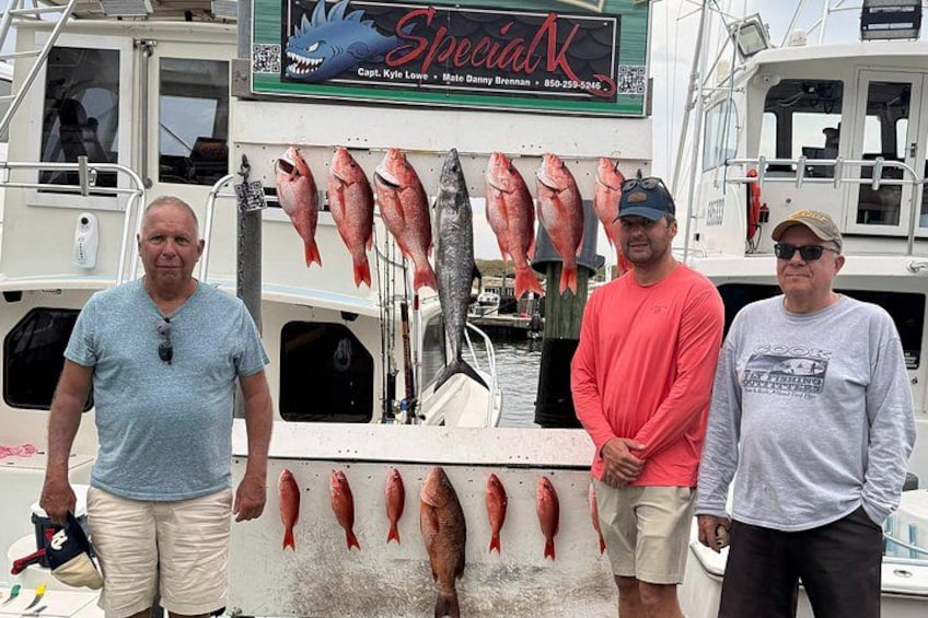 Three people standing on a boat with several fish displayed on the side. 2