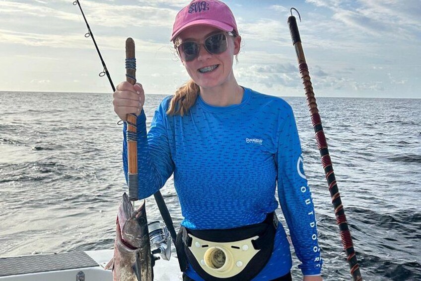 A person holding a fish and a fishing rod on a boat. 3