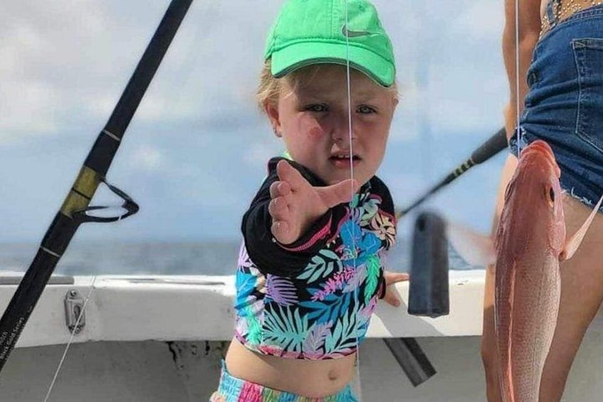 A child on a boat wearing a colorful swimsuit and a green cap, holding a fishing rod. 1