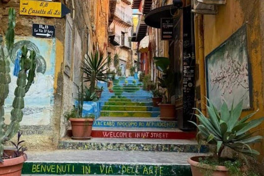 Una calle estrecha con escaleras que conducen a un edificio, plantas en macetas y letreros en un idioma extranjero. 3