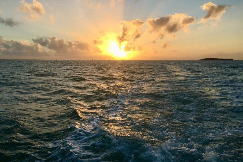 A sunset over the ocean with waves and a distant island. 4
