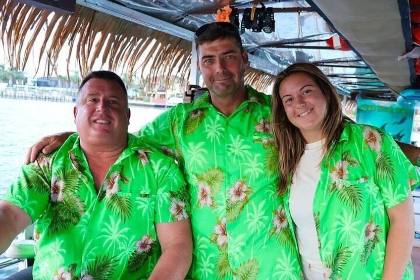 Tres personas en un bote, vistiendo camisas tropicales verdes a juego. 3