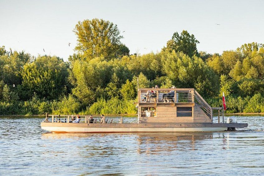 A wooden boat with a deck and railing, floating on calm water with trees in the background. 3