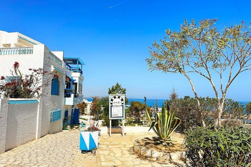 A coastal building with a blue and white facade, a paved entrance, and a clear view of the sea. 3