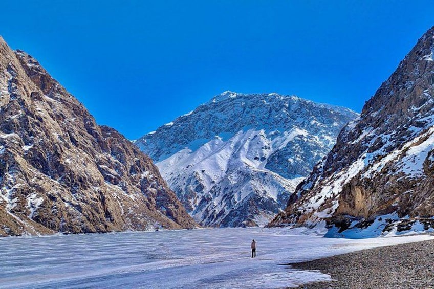 Un glaciar con una persona de pie, rodeado de montañas rocosas y nieve. 2