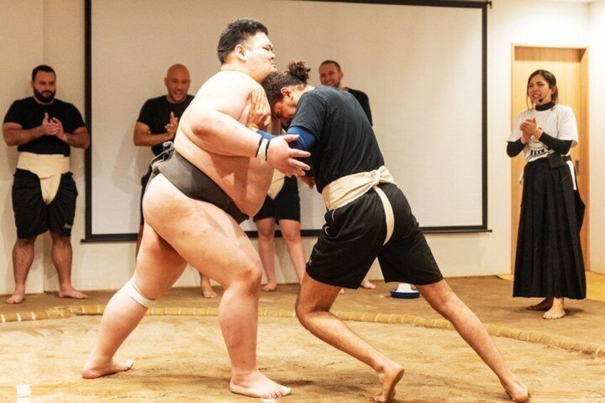 Two sumo wrestlers in a match, with an audience watching. 2