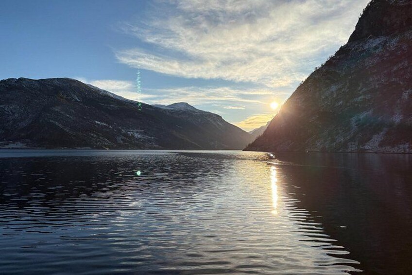 A calm lake with mountains in the background and the sun setting on the horizon. 4