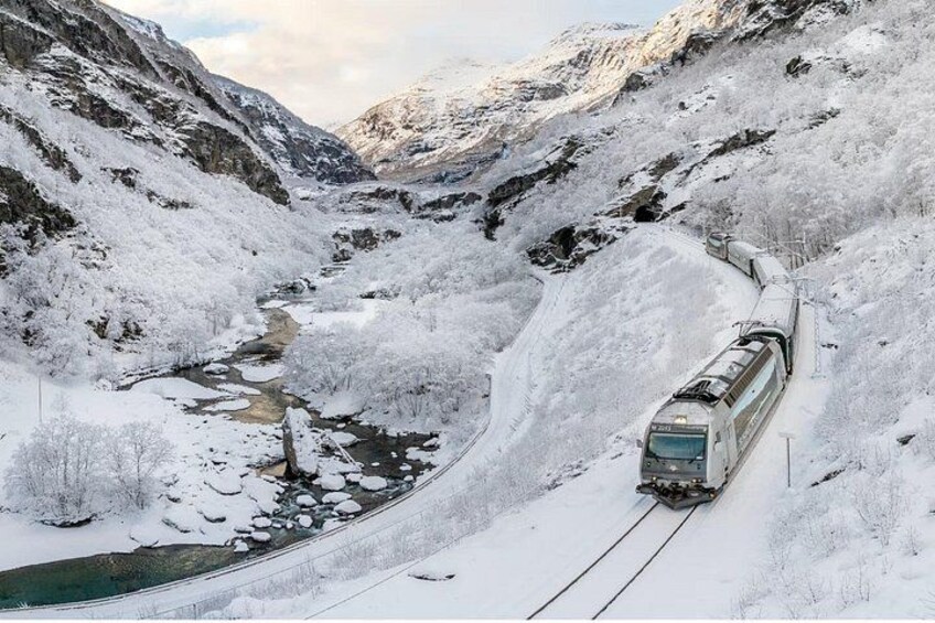 A train traveling through a snowy mountainous landscape with a river. 1