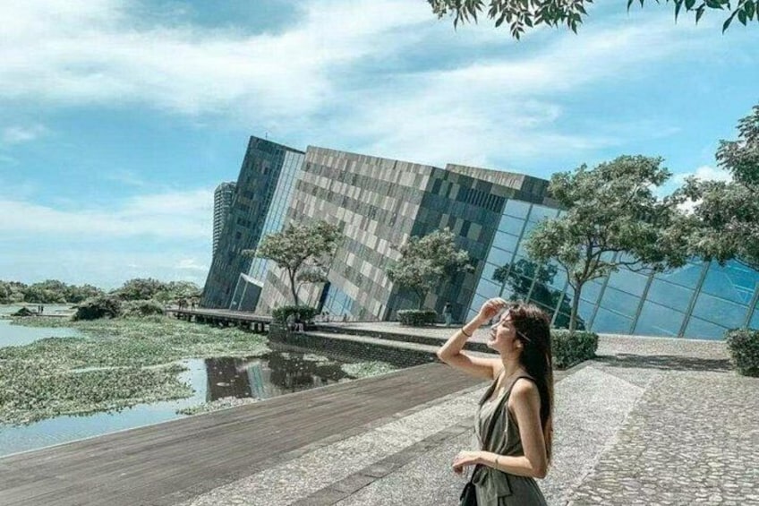 A modern building with a reflective glass facade, a paved walkway, and a body of water with lily pads. 5