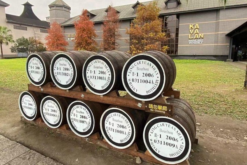 A stack of whiskey barrels with labels, a sign reading 'No Climbing,' and a building with a sign that says 'KAVALAN WHISKEY DISTILLERY.' 4