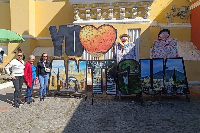 Una señal de calle con las palabras 'YO' y 'LOVE' en letras grandes, y un símbolo de corazón. Varias pinturas se ven sobre caballetes al fondo. 1