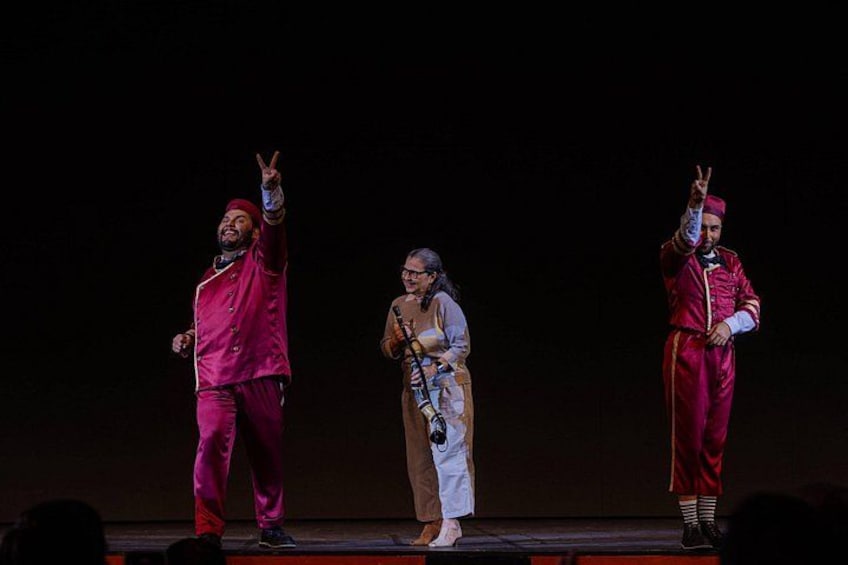 Three people on a stage, one in a pink suit and the other in a red suit, both making a peace sign. 5