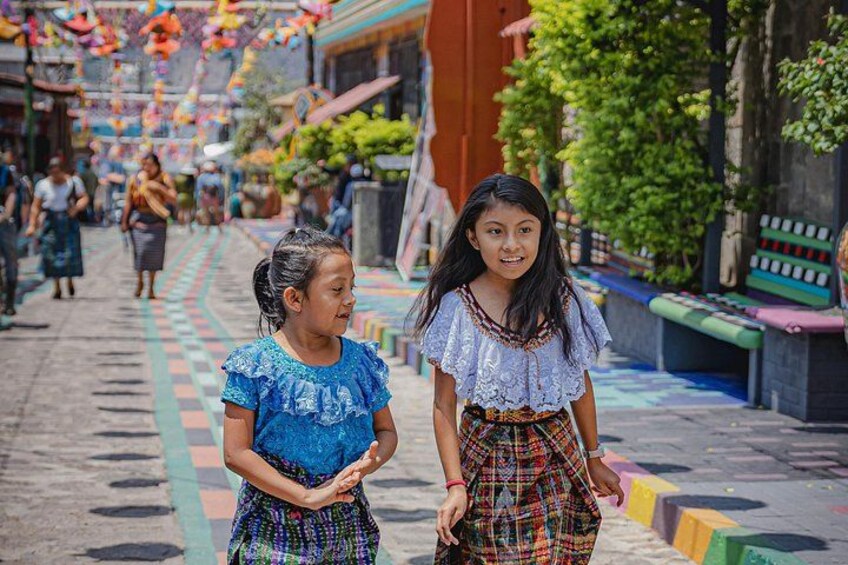 Dos niños caminando por una calle colorida con pavimento estampado y edificios al fondo. 2