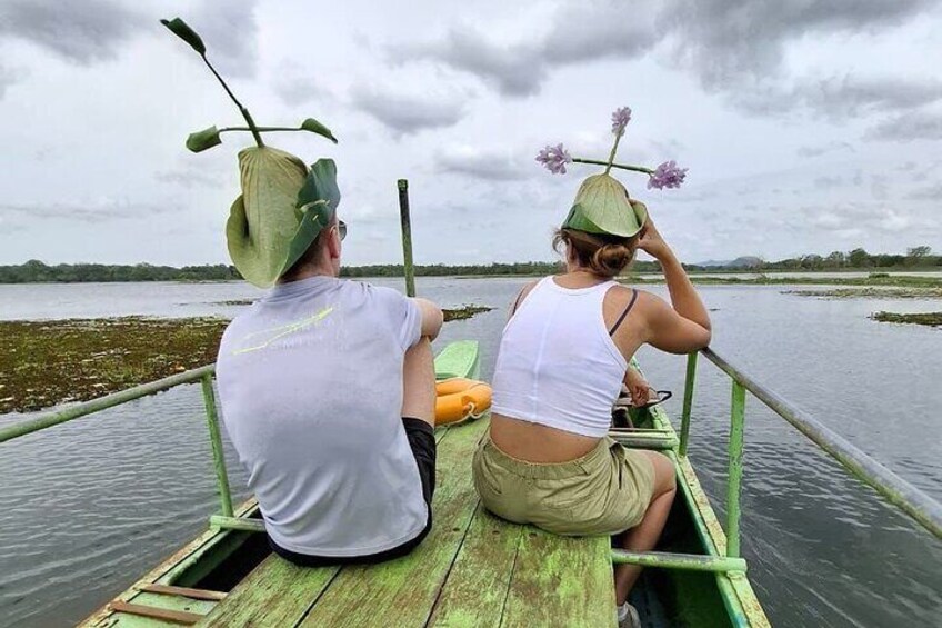 Two people in a green boat on a calm body of water, wearing hats with leaves. 4