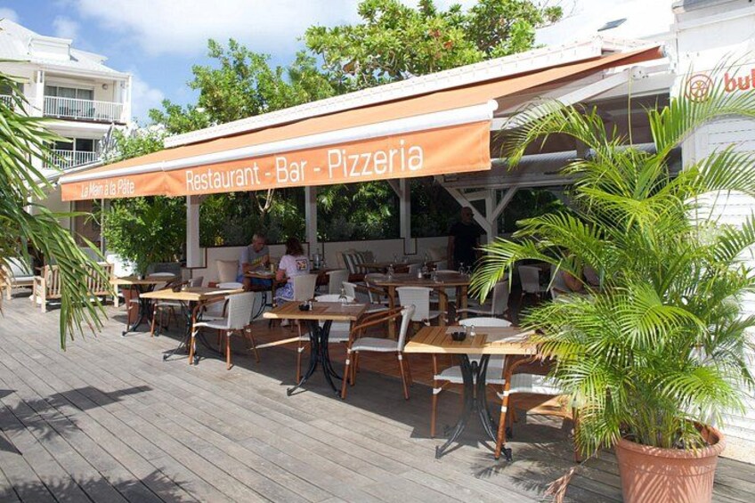 Un restaurante al aire libre con terraza cubierta, mesas y sillas de madera, y plantas en macetas. 3