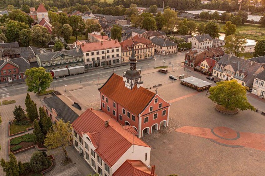 A town square with historic buildings, a prominent church, and a large tree. 3