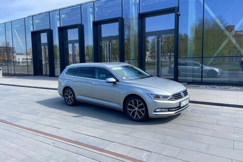 A silver station wagon parked in front of a modern glass building. 2