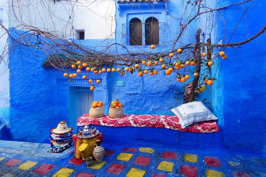 Un patio azul vibrante con naranjas colgando de un árbol, un tapete tradicional marroquí y un montón de cestas tejidas de colores. 2