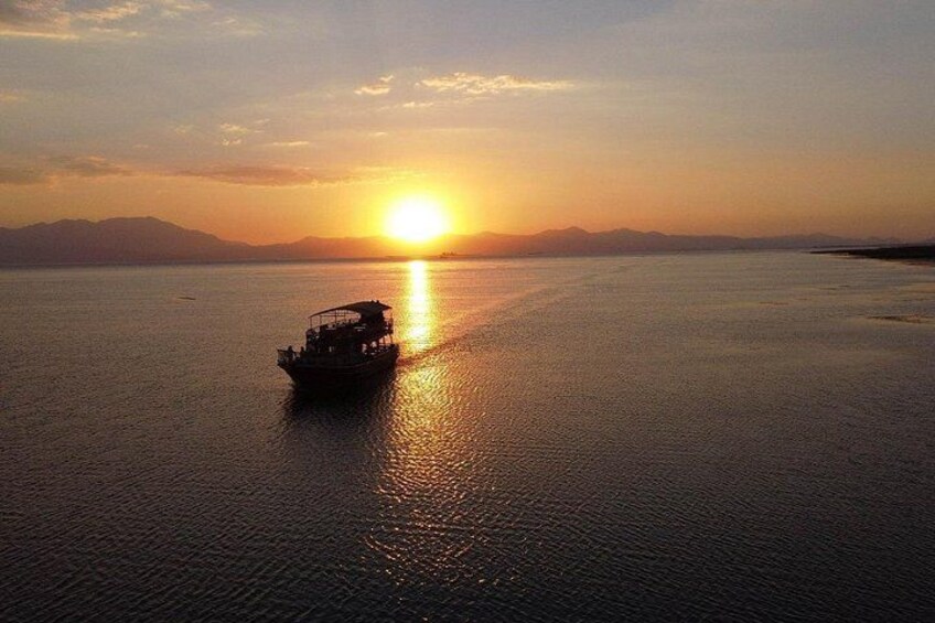 A boat on calm water during sunset with a mountain range in the background. 5