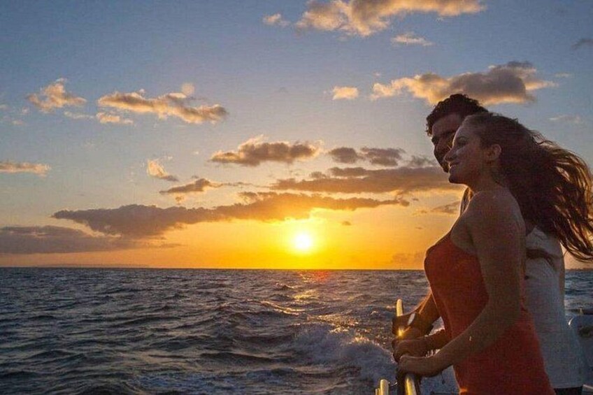 A couple standing on a boat with the sunset in the background. 1