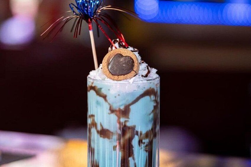 A tall glass with a layered drink, topped with a cookie and a decorative stick. 3