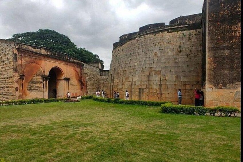 Un muro de piedra histórico con una entrada arqueada, un patio cubierto de césped y algunas personas caminando. 5