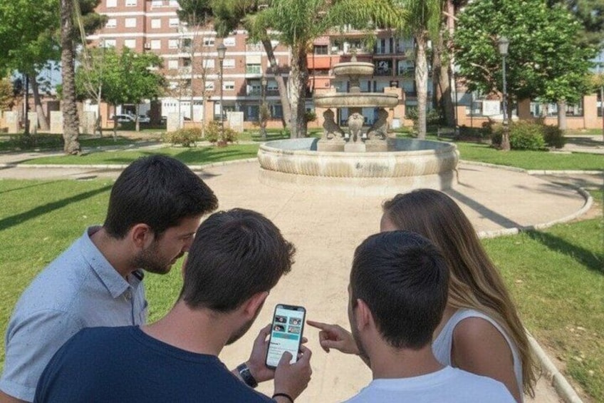 Three people standing by a fountain in a park with buildings in the background. 5