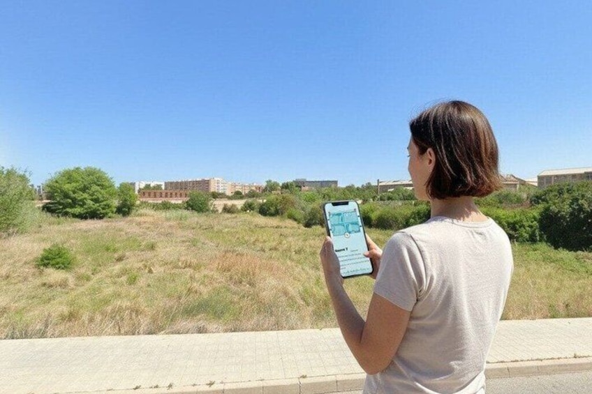 A person using a smartphone outdoors, with a building complex in the background. 2
