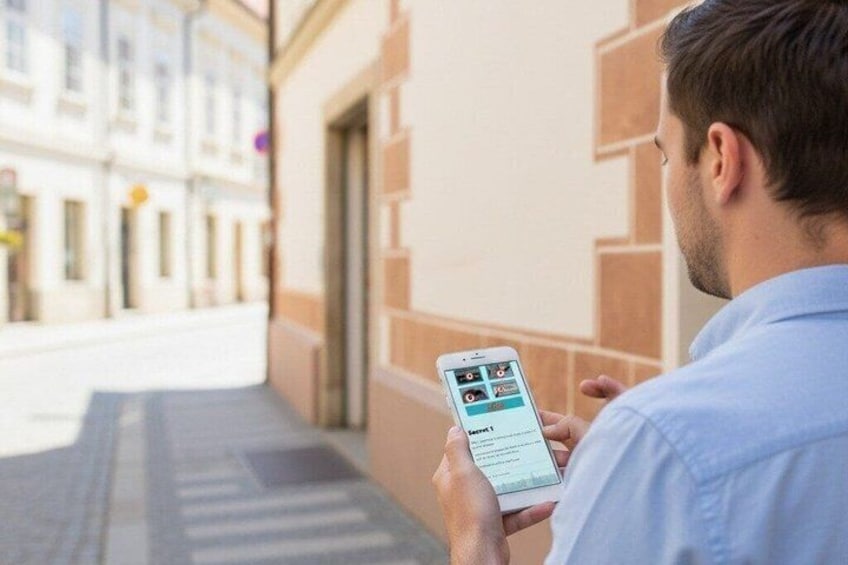 A person holding a smartphone, standing on a sidewalk with buildings in the background. 4