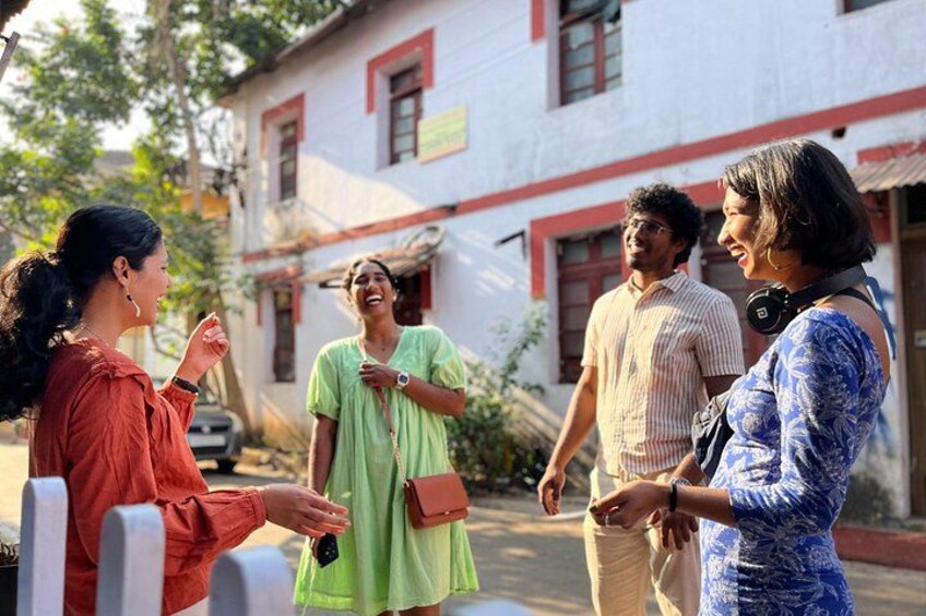 A group of people standing outdoors in front of a building with red trim. 4