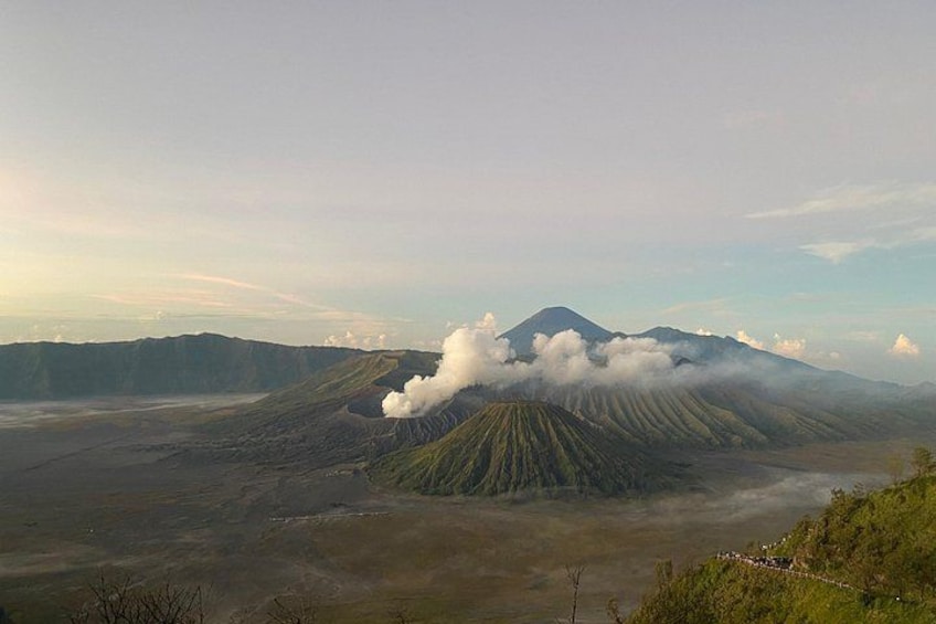 A volcano with smoke, a valley, and distant mountains. 2