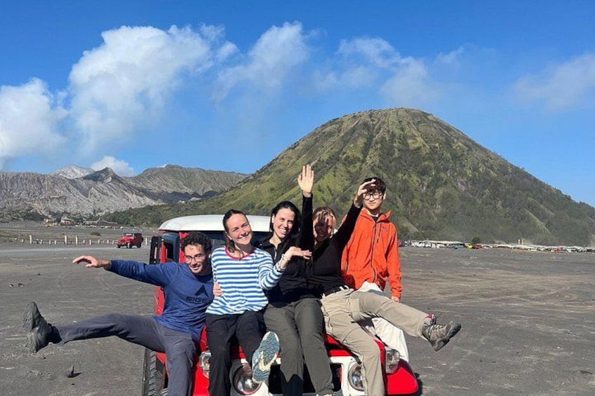 Four people on a red vehicle with a mountain in the background. 1