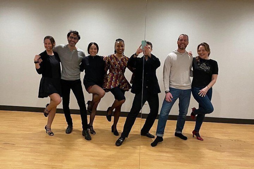A group of people in a dance studio with wooden floors and a mirror wall. 5