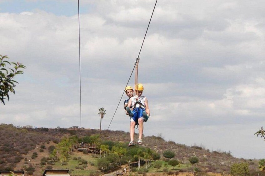 A person on a zip line with a harness, wearing a helmet, and a guide standing on the ground. 5