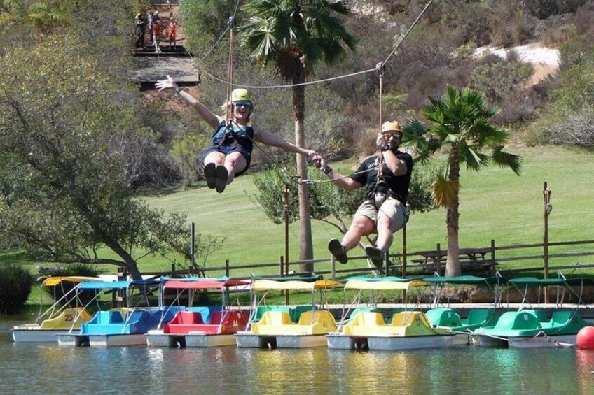 Two people zip-lining over a body of water with colorful boats docked below. 3