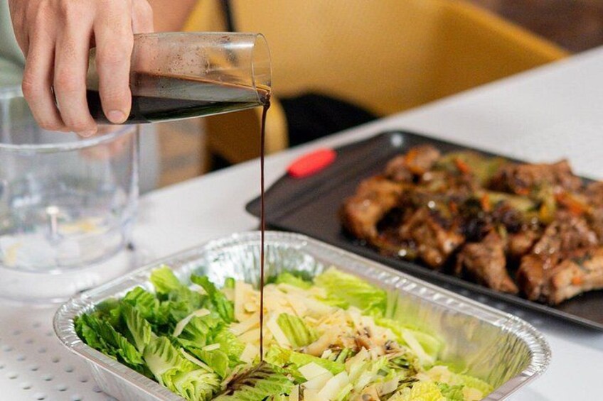 Una persona vertiendo un líquido oscuro, posiblemente salsa de soja, sobre una ensalada y carne a la parrilla. 3