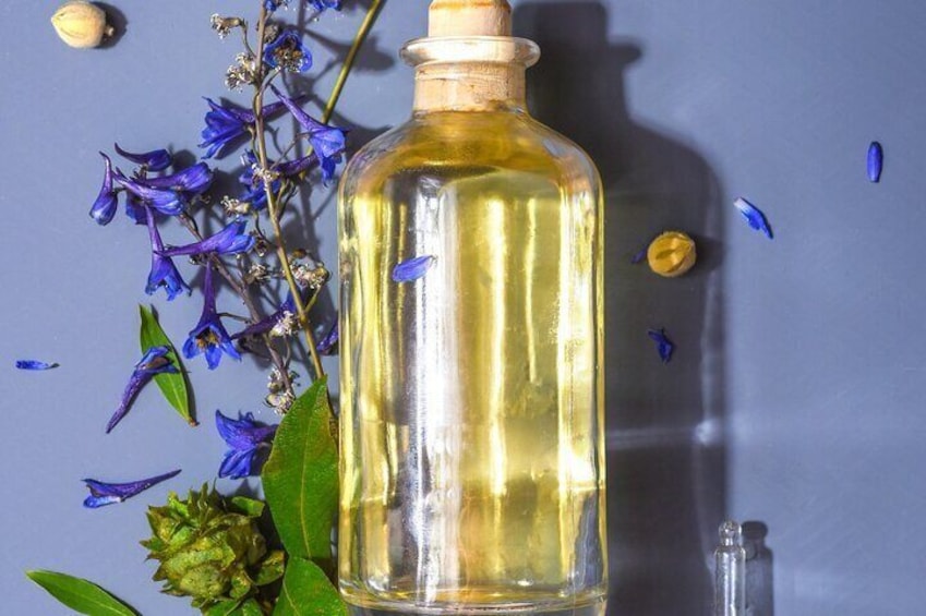 A clear glass bottle with a wooden cap, surrounded by blue flowers and green leaves. 1