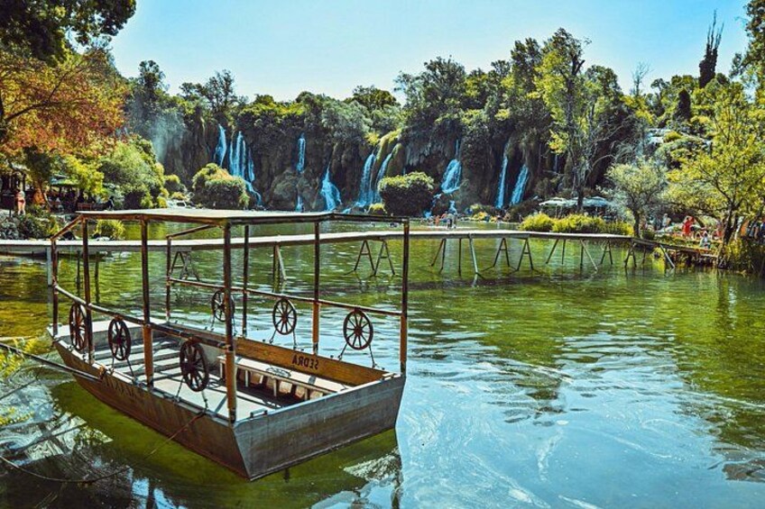 Una barca de madera con ruedas en un río tranquilo, rodeada de exuberante vegetación y cascadas al fondo. 4