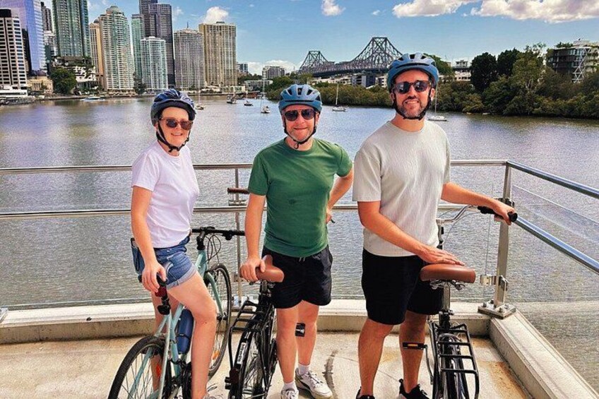 Three people on a boat with bicycles, a river, and a city skyline in the background. 3