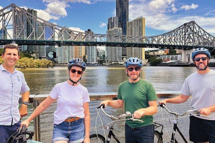 Four people on bicycles with a river and bridges in the background. 2