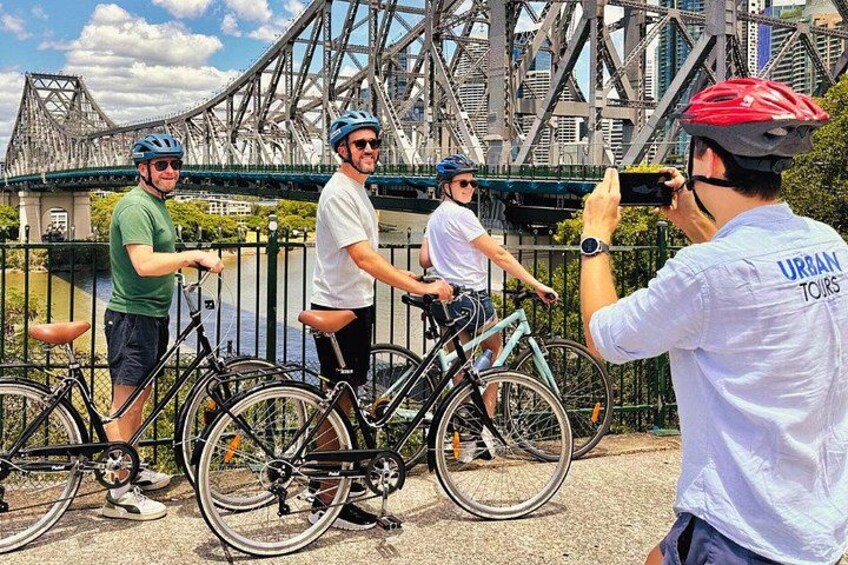 A group of cyclists near a bridge with a photographer. 1