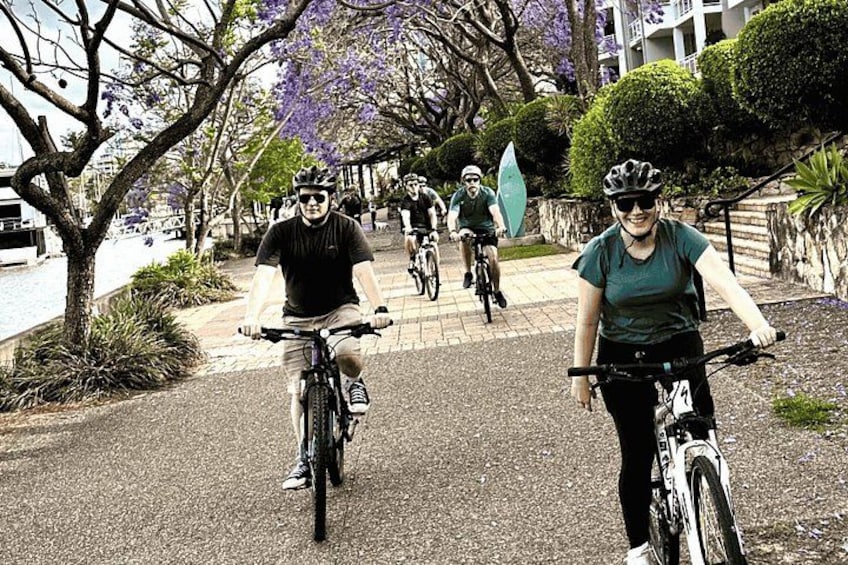 A group of cyclists on a paved path with trees and a building in the background. 4