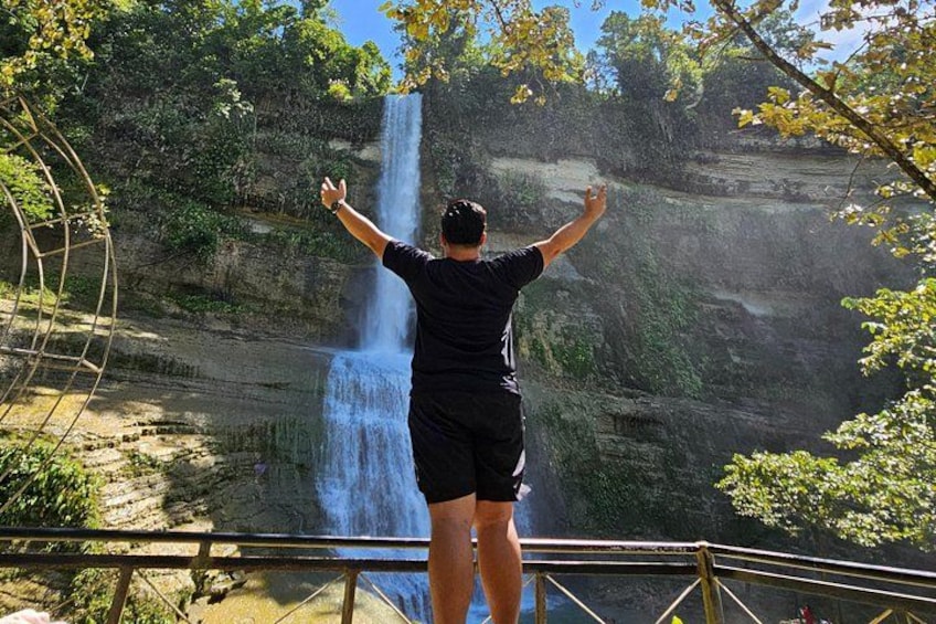 A person standing on a platform with arms raised, overlooking a waterfall. 4