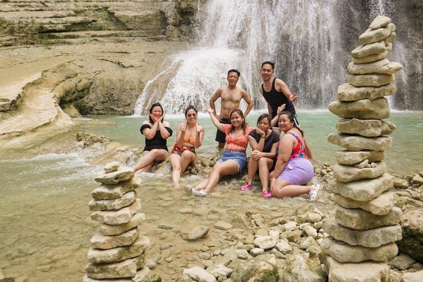A group of people sitting by a waterfall in a natural setting with stacked stones. 1