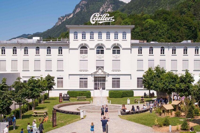 A large white building with arched windows and a Coca-Cola sign, surrounded by a landscaped garden and a mountainous backdrop. 5