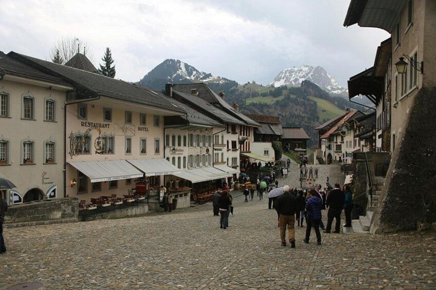 A cobblestone street in a mountainous village with buildings labeled 'Restaurant' and 'Hotel.' 3
